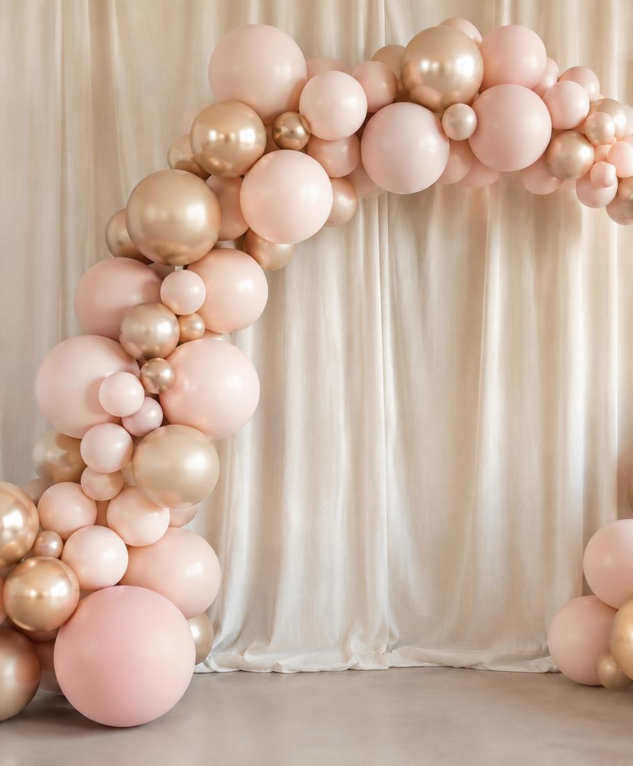 Blush and champagne balloon arch in front of a neutral fabric backdrop